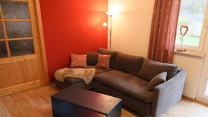 A living room with a brown sofa, a wooden coffee table, a red wall, a window with curtains, and a lamp. - Holiday home at Maxschacht (Stockheim)