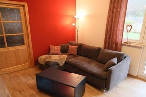 Ein Wohnzimmer mit einem braunen Sofa, einem Holztisch, einer roten Wand, einem Fenster mit Vorhängen und einer Lampe.