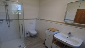 A bathroom with a glass-enclosed shower, a toilet, and a sink with a mirror above. - Holiday home at Maxschacht (Stockheim)