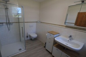 Ein Badezimmer mit Duschkabine, Toilette und Waschbecken mit Spiegel darüber.