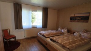 A room with two beds, a chair, a window with curtains, and a radiator. - Holiday home at Maxschacht (Stockheim)