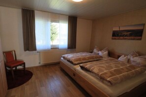 Ein Zimmer mit zwei Betten, einem Sessel, einem Fenster mit Vorhängen und einer Heizung.