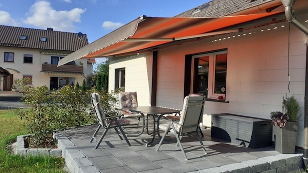 An outdoor patio with a table and chairs, a covered seating area, and a small garden. - Holiday home at Maxschacht (Stockheim)