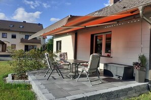 An outdoor patio with a table and chairs, a covered seating area, and a small garden. - Holiday home at Maxschacht (Stockheim)