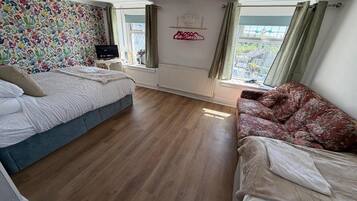 A bedroom with two beds, a radiator, a window with curtains, and a wall with a floral pattern.