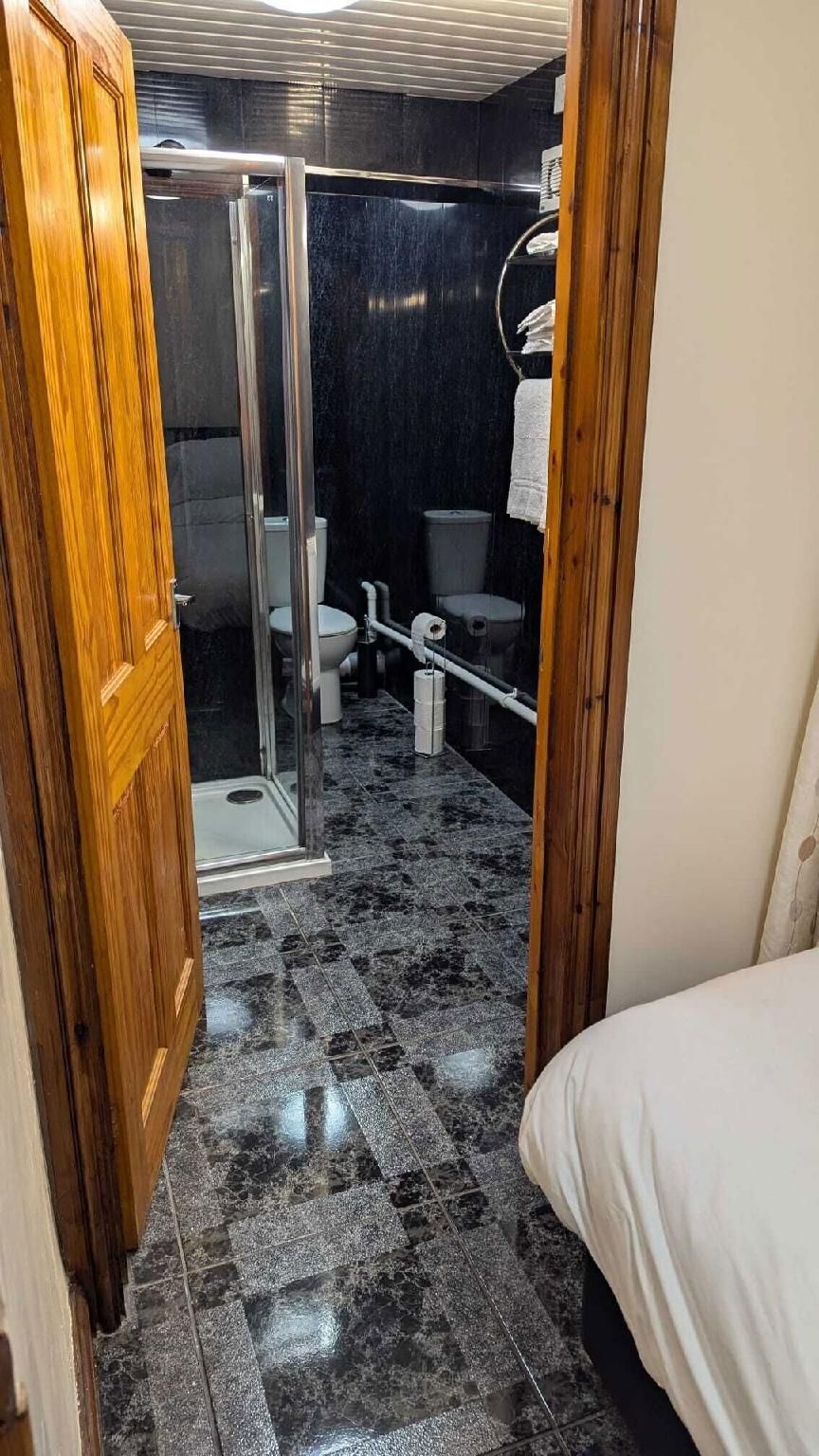 A narrow hallway leading to a bathroom with a shower, toilet, and bidet.