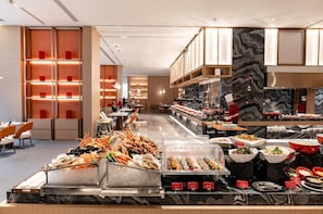 A buffet area with seafood and various dishes, a kitchen in the background, and a modern interior design. - LN Dongfang Hotel Nansha (Guangzhou)