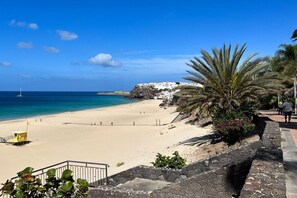 A beach with a lifeguard tower, a clear sky, and a building on a cliff. - Apartment in Morro Jable with swimming pool (Morro Jable)