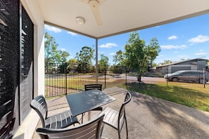 A covered outdoor seating area with a table and chairs, a view of a street with cars, and a building in the background. - Spacious 3-bed Family Retreat in Darwin (Darwin)