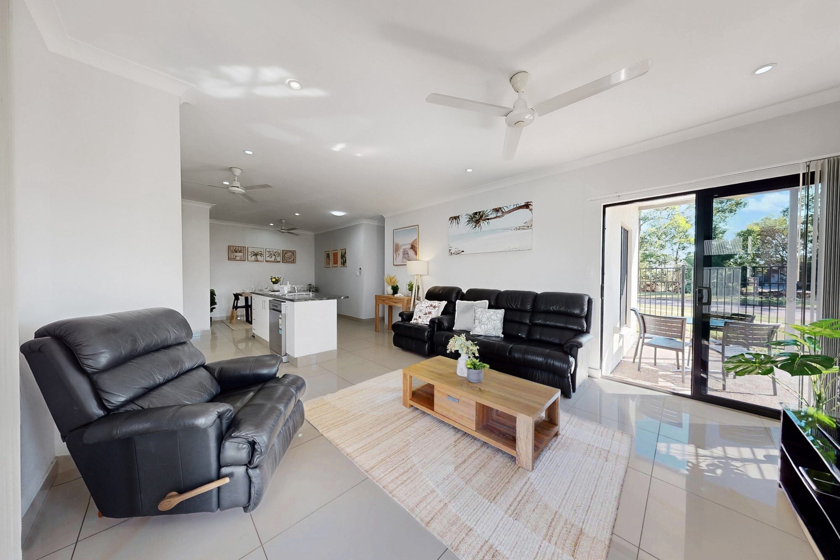 A modern living room with a black leather sofa, a wooden coffee table, and a ceiling fan.