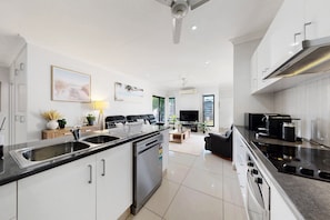 A modern kitchen with stainless steel appliances, a dining area with a sofa and coffee table, and a living room with a TV and seating. - Spacious 3-bed Family Retreat in Darwin (Darwin)