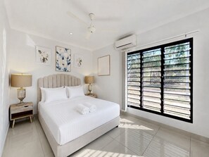 A hotel room with a large bed, two bedside tables, a ceiling fan, an air conditioning unit, and a window with blinds. - Spacious 3-bed Family Retreat in Darwin (Darwin)