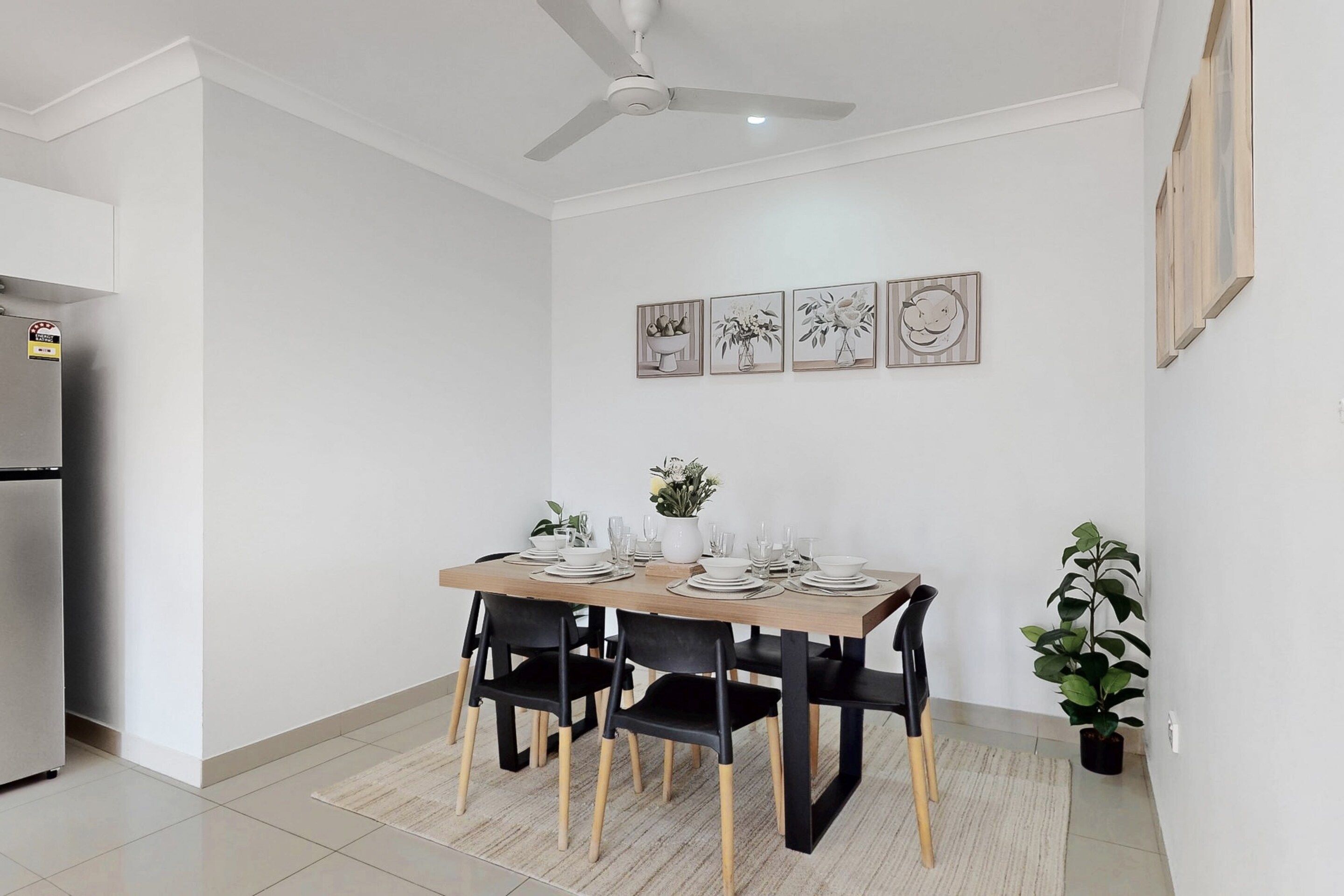 A dining area with a table set for four, black chairs, a ceiling fan, and framed artwork on the wall.