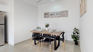 Un coin repas avec une table dressée pour quatre personnes, des chaises noires, un ventilateur de plafond et des œuvres d’art encadrées accrochées au mur.