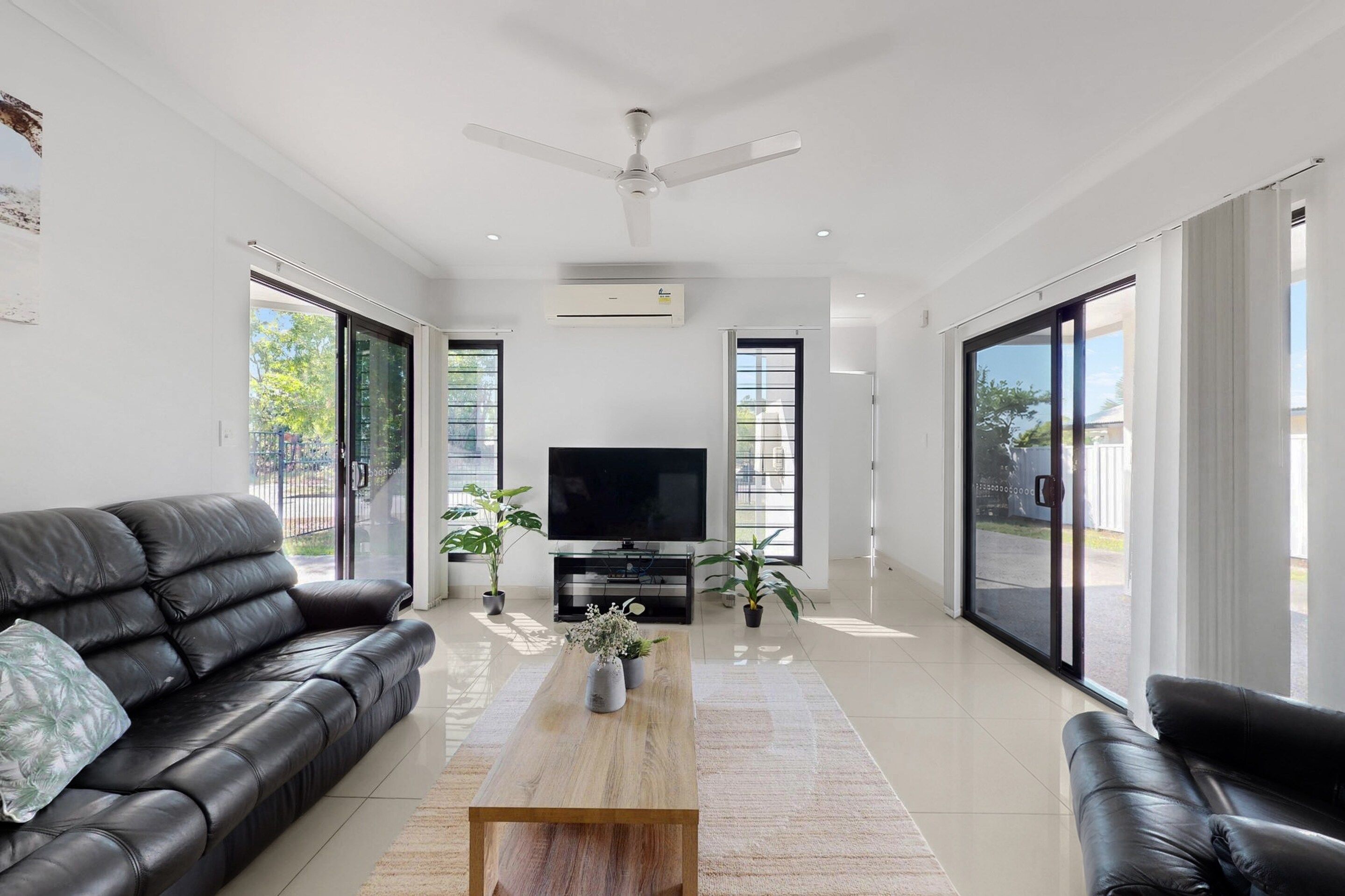 A modern living room with a black leather sofa, a wooden coffee table, a flat-screen TV, and large sliding glass doors.