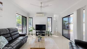 A modern living room with a black leather sofa, a wooden coffee table, a flat-screen TV, and large sliding glass doors.