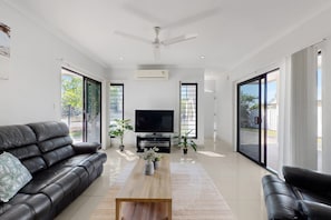 A modern living room with a black leather sofa, a wooden coffee table, a flat-screen TV, and large sliding glass doors. - Spacious 3-bed Family Retreat in Darwin (Darwin)