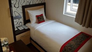 A single bed with a red accent pillow, a bedside table with a lamp, and a window with curtains. - Treeli Boutique Hotel (Bukittinggi)