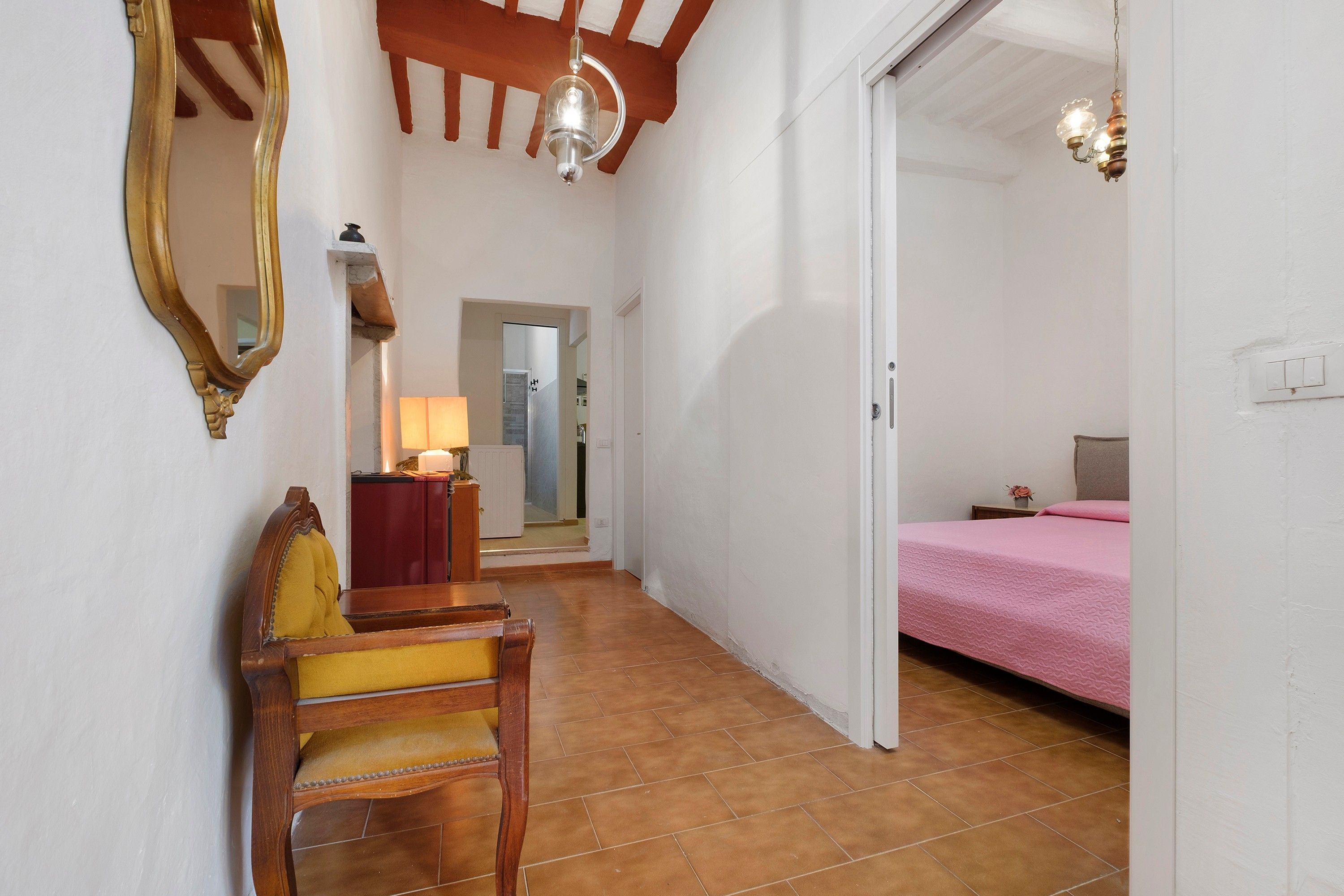 Ein Schlafzimmer mit einem Bett, einem Sessel, einem Schreibtisch, einem Spiegel und einer Tür zu einem anderen Raum.