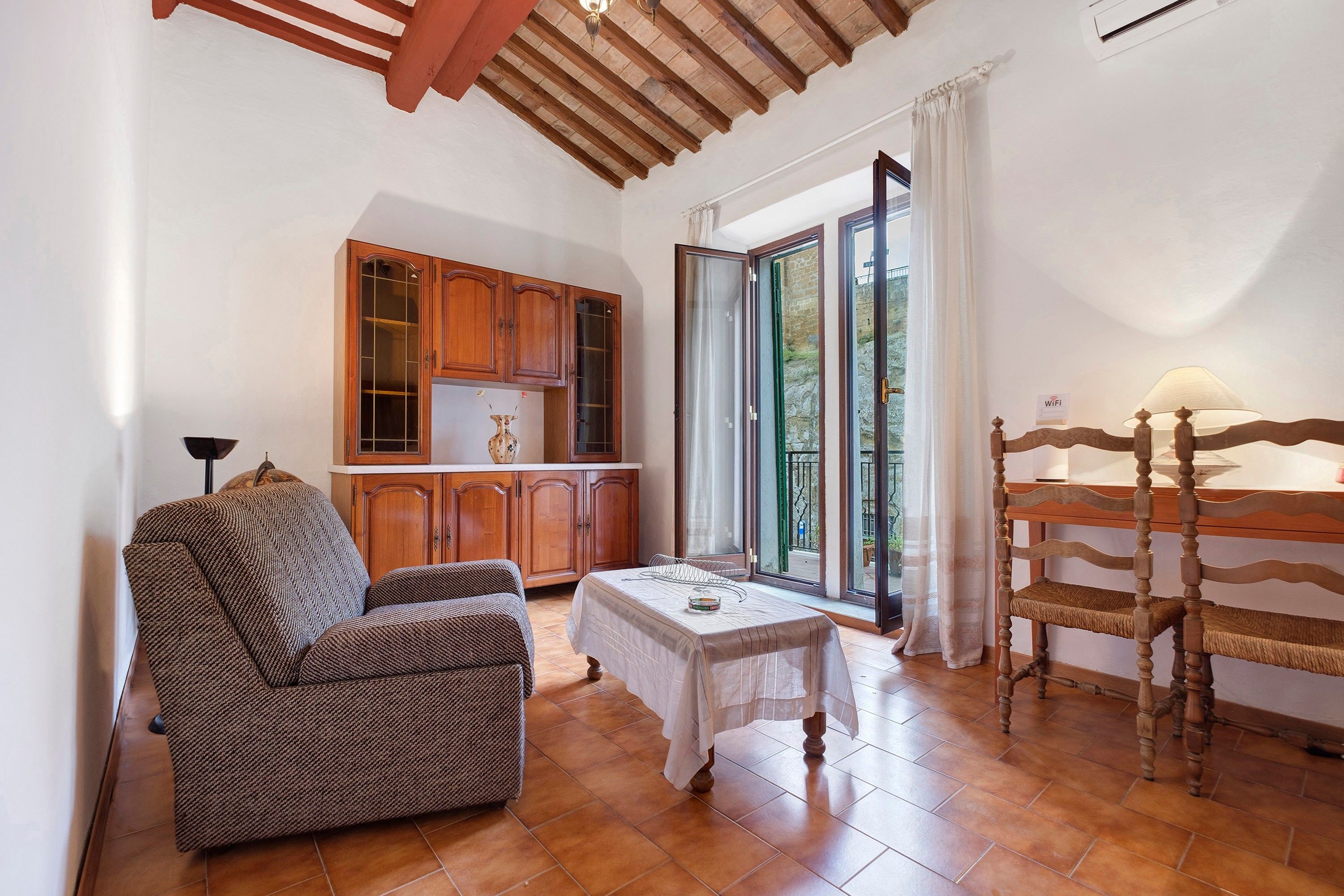 Un accogliente soggiorno con divano, tavolo da pranzo e sedia in legno. Si nota una cucina con mobili in legno e una finestra vista.