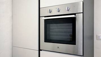 Horno de acero inoxidable con panel de control digital y puerta de vidrio, instalado en una cocina con armarios blancos.