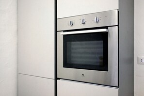 Forno de aço inoxidável com painel de controle digital e porta de vidro, instalado em cozinha com armários brancos.
