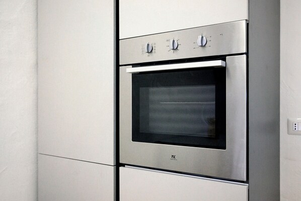 A stainless steel oven with a digital control panel and a glass door, installed in a kitchen with white cabinetry.