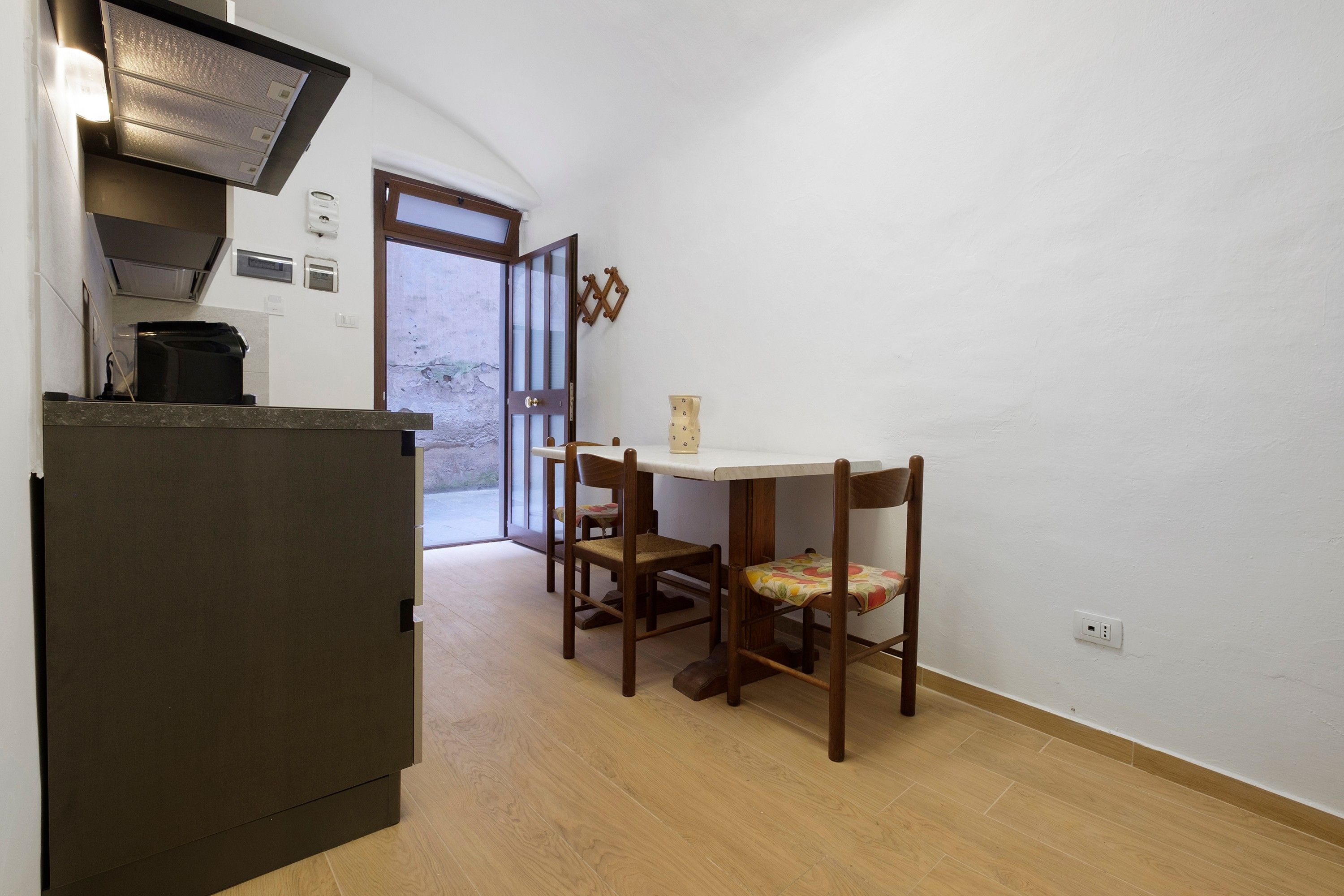 Una cucina compatta con piano cottura integrato, un tavolo da pranzo con due sedie e una porta che dà su una zona esterna.