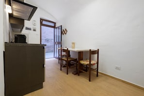 Una cucina compatta con piano cottura integrato, un tavolo da pranzo con due sedie e una porta che dà su una zona esterna.