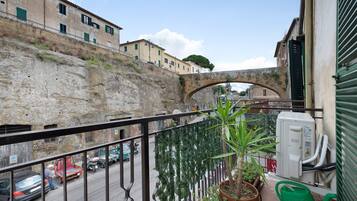 A balcony with a view of a stone wall, a street with cars, and a building with a green awning.