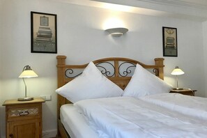 Un lit bien fait, avec du linge de lit blanc, deux lampes de chevet et des œuvres d’art encadrées accrochées aux murs.