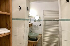 Une salle de bain avec une étagère en bois, un lavabo en céramique verte, un porte-serviettes et un autre porte-serviettes avec une serviette.