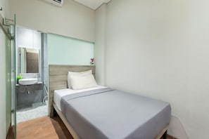 Una camera d'albergo moderna con un letto, un bagno con uno specchio e una piccola finestra.