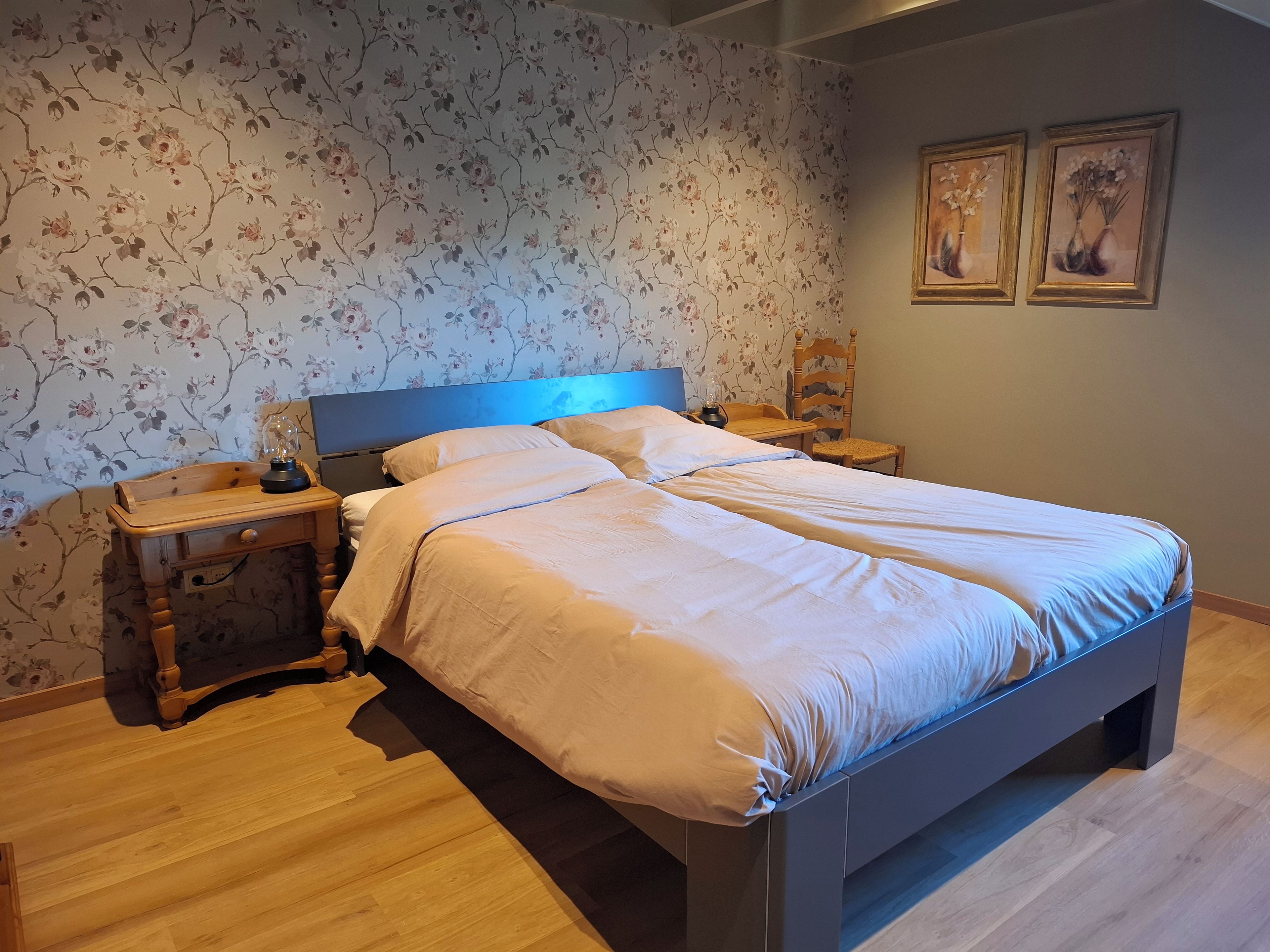 A bedroom with a bed, nightstands, a lamp, and floral wallpaper.