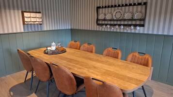 A dining area with a long wooden table, six brown chairs, and a wall-mounted display of plates and cups.