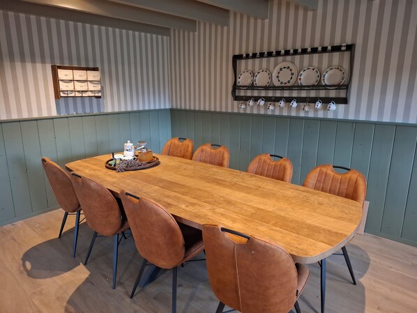 A dining area with a long wooden table, six brown chairs, and a wall-mounted display of plates and cups. - Vrbo Property (Aarle-Rixtel)