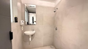 Un baño con un lavamanos blanco, un cabezal de ducha de mano y un espejo.