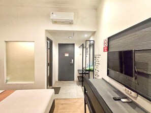 Habitación de hotel con una cama, un escritorio con televisor, un espejo y una puerta que da a otra habitación.