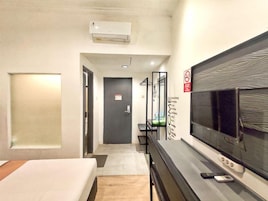 Habitación de hotel con una cama, un escritorio con televisor, un espejo y una puerta que da a otra habitación.