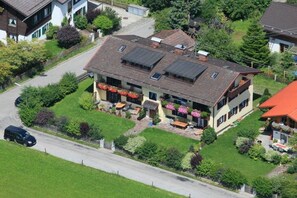 Ein zweigeschossiges Haus mit einem geneigten Dach, Solaranlagen und einer Veranda mit Sitzgelegenheit im Freien.