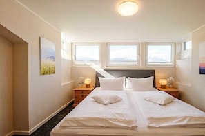 Ein Hotelzimmer mit einem großen Bett, zwei Nachttischen und drei Fenstern.