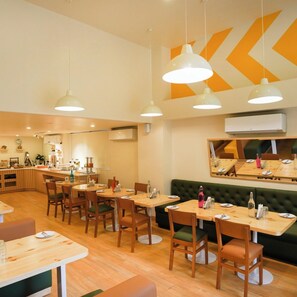 En restaurang med träbord och stolar, en bardisk och en grön, vadderad sittgrupp.