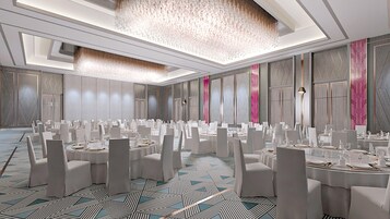 Un amplio salón de banquetes con mesas redondas, sillas blancas y una alfombra estampada.