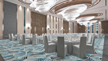 Un amplio salón de banquetes con mesas redondas, sillas blancas y modernas lámparas de araña.