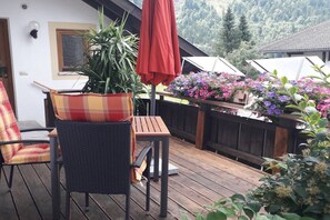 An outdoor patio with a table and chairs, a potted plant, and a wooden fence with flowers. - Holiday apartment in Ettal with barbecue (Ettal)