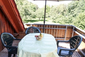 Eine Terrasse im Freien mit Tisch, der mit einer weißen Tischdecke bedeckt ist, umgeben von Stühlen und einem Holzzaun im Hintergrund.