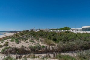 A coastal landscape with a sandy beach, a wooden fence, and modern buildings in the background.