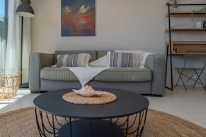 A living room with a grey sofa, a round black coffee table with a woven placemat, and a large abstract painting on the wall.