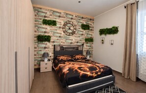 Ein modernes Schlafzimmer mit Ziegelwand, einem Bett mit schwarzem und orangefarbenen Muster, Nachttischen mit Lampen und zwei Wandpflanzgefäßen.