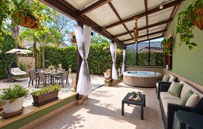 Eine überdachte Terrasse im Freien mit Whirlpool, Sitzgelegenheit und Pflanzen in Töpfen.